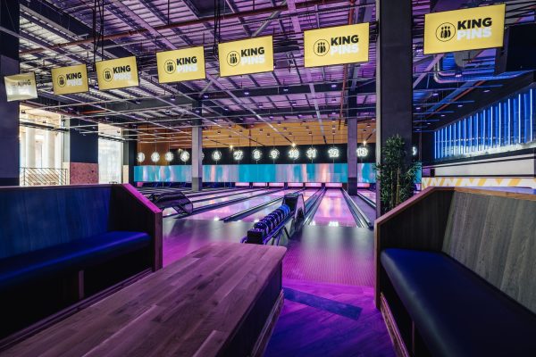 A dark room of empty bowling alleys lit up with pink light.